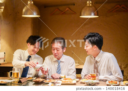 一位年輕員工在居酒屋（日本酒吧）為資深同事倒酒。 140018416