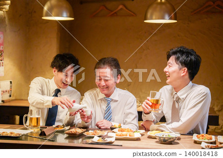 一位年輕員工在居酒屋（日本酒吧）為資深同事倒酒。 140018418