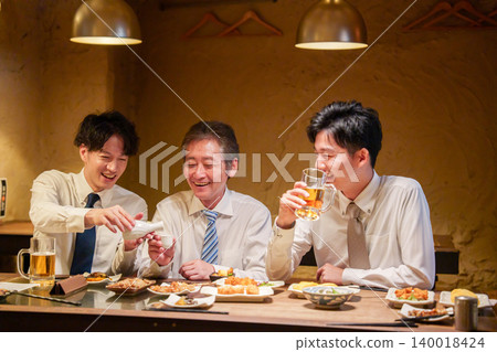 一位年輕員工在居酒屋(日本酒吧)為資深同事倒酒。 一位年輕員工在居酒屋(日本酒吧)為資深同事倒酒。 140018424