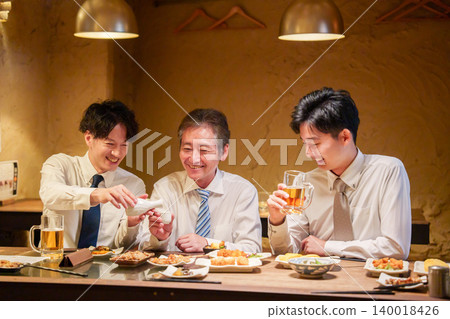 一位年輕員工在居酒屋(日本酒吧)為資深同事倒酒。 一位年輕員工在居酒屋(日本酒吧)為資深同事倒酒。 140018426