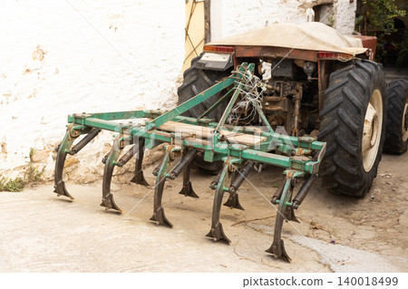 Green Cultivator Tines Attached to Red Tractor in Rural Village Yard Green Cultivator Tines Attached to Red Tractor in Rural Village Yard 140018499
