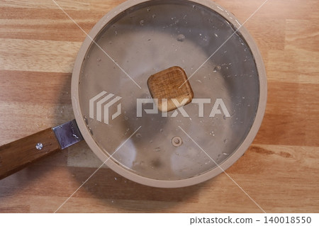 Pot with Glass Lid on Wooden Surface Pot with Glass Lid on Wooden Surface 140018550