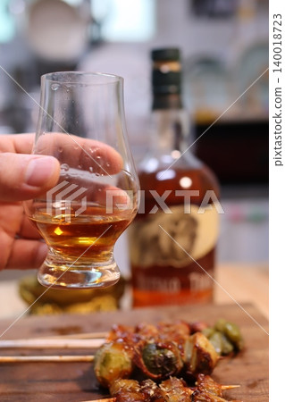 Hand Holding Whiskey Glass with Bottle and Food Background Hand Holding Whiskey Glass with Bottle and Food Background 140018723