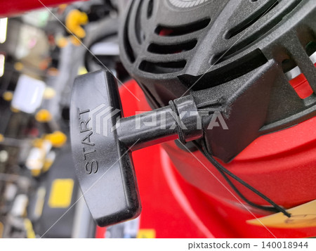 A bright red lawnmower with a shiny pull-start mechanism sits ready for action 140018944