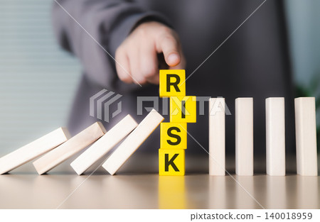 Risk management and prevention concept. Person stopping falling dominoes with yellow blocks spelling "RISK" symbolizing risk management, prevention, strategic decision-making in business operations, Risk management and prevention concept. Person stopping falling dominoes with yellow blocks spelling "RISK" symbolizing risk management, prevention, strategic decision-making in business operations, 140018959