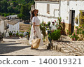 Woman traveling in a small Spanish village with straw hat and basket on a sunny day 140019321