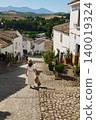 Woman traveling through a small Spanish village with cobblestone streets and mountain views 140019324
