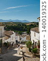 Woman enjoying a sunny stroll through a small Spanish village with mountain views 140019325