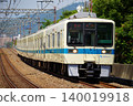 Odakyu 8000 series train speeds along a straight stretch of track in a leafy suburban area. 140019918