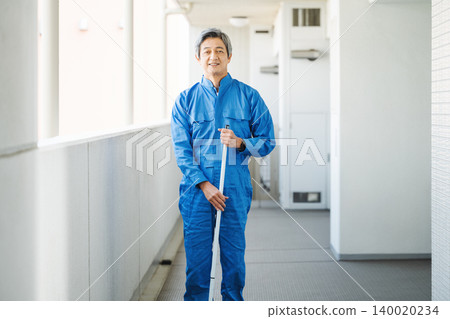 一位資深的男性建築管理員正在清潔公寓大樓的地板。 140020234