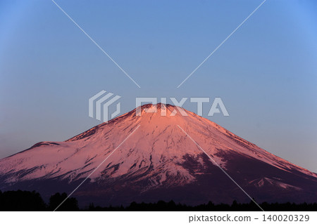 Mount Fuji, with its slightly pinkish snow-capped peak, sits majestically against a sky full of light blue. Mount Fuji, with its slightly pinkish snow-capped peak, sits majestically against a sky full of light blue. 140020329