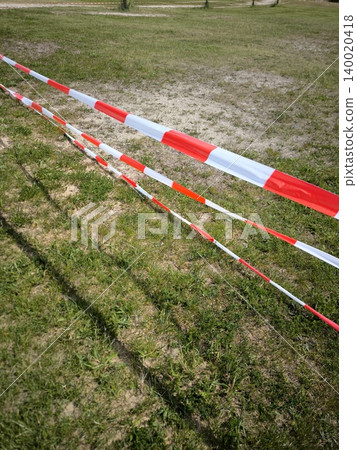 Red-and-white warning tape against a background of green grass. Red-and-white warning tape against a background of green grass. 140020418