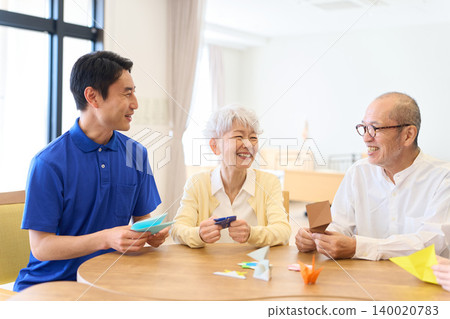 Seniors and caregivers folding origami at a nursing home. 140020783