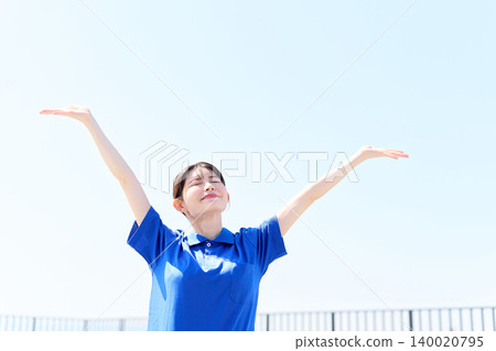 An Asian female caregiver raises both hands to the blue sky. 140020795