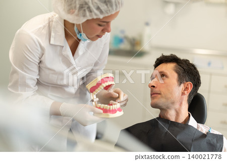 Young female dentist showing model of teeth to patient Young female dentist showing model of teeth to patient 140021778