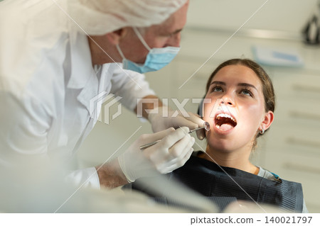 Mature man doctor dentist in white coat examines oral cavity of girl patient in dentistry. Mature man doctor dentist in white coat examines oral cavity of girl patient in dentistry. 140021797