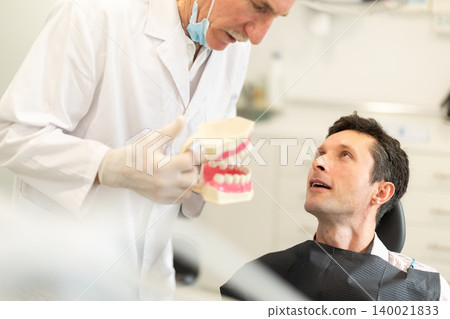 Senior man dentist communicates with male patient, shows model of jaws Senior man dentist communicates with male patient, shows model of jaws 140021833