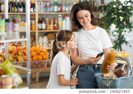 Girl with mother customers at shop scans QR code on juice package using phone camera Girl with mother customers at shop scans QR code on juice package using phone camera 140021947