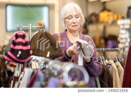 Eldery woman chooses hat in accessories store Eldery woman chooses hat in accessories store 140021956