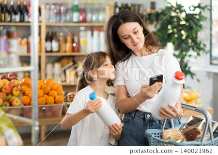 Checking expiration date of milk - mother and daughter checking qr code on bottle of milk Checking expiration date of milk - mother and daughter checking qr code on bottle of milk 140021962