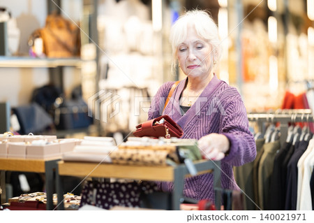 Attentive mature woman choosing wallet in clothing store Attentive mature woman choosing wallet in clothing store 140021971