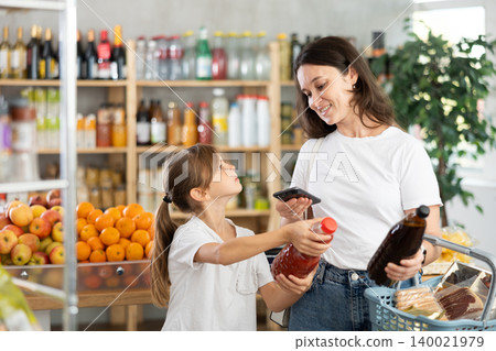 Girl with mother customers at shop scans QR code on juice package using phone camera Girl with mother customers at shop scans QR code on juice package using phone camera 140021979
