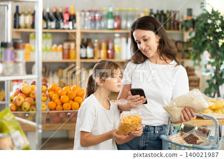 Mother and daughter checks expiration date of cornflakes and oat flakes - scans QR code on label Mother and daughter checks expiration date of cornflakes and oat flakes - scans QR code on label 140021987