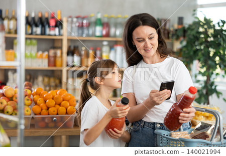 Mother and daughter choose bottles of juice and scan QR code with smartphone in supermarket Mother and daughter choose bottles of juice and scan QR code with smartphone in supermarket 140021994