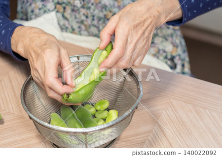一位老婦人正在剝蠶豆。家常菜,食材準備。 一位老婦人正在剝蠶豆。家常菜,食材準備。 140022092