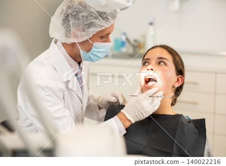 Adult male dentist examining female patient 140022216