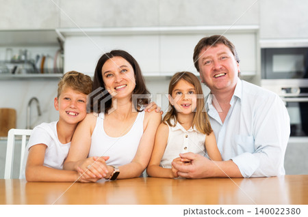 Parents posing with their two little children by the table in the kitchen Parents posing with their two little children by the table in the kitchen 140022380
