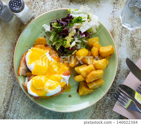 Eggs Benedict with smoked salmon, fried potatoes and greens Eggs Benedict with smoked salmon, fried potatoes and greens 140022384