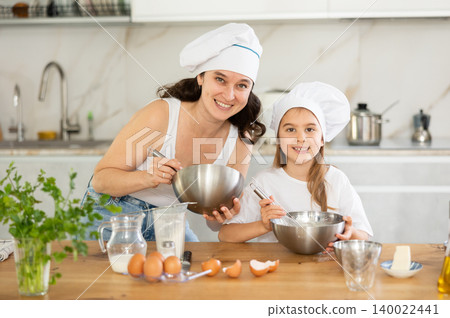 Happy mother and her daughter whisking ingredients in metal bowl in the kitchen Happy mother and her daughter whisking ingredients in metal bowl in the kitchen 140022441