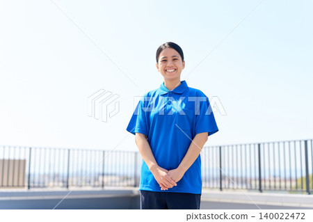 A foreign female caregiver standing against a blue sky. 140022472