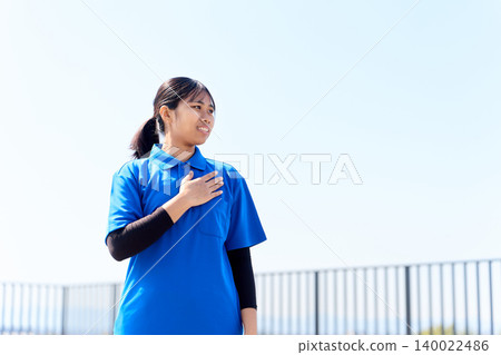 A female caregiver places her hand on her chest against a blue sky backdrop. 140022486