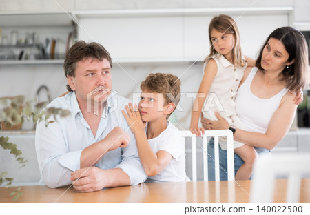 Offended father sitting at the kitchen table being hugged by son 140022500