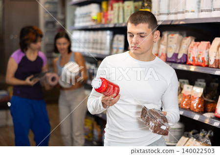 Focused young guy choosing high-protein bread and supplement in sports nutrition store Focused young guy choosing high-protein bread and supplement in sports nutrition store 140022503