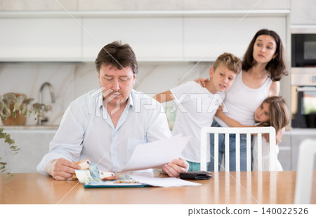 Frustrated husband is sitting in kitchen and carefully reading loan agreement. 140022526