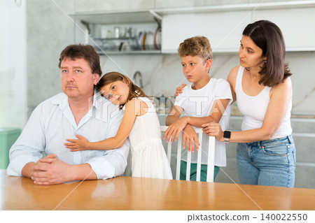 Frustrated man sits at kitchen table and tells wife and children about unforeseen difficulties Frustrated man sits at kitchen table and tells wife and children about unforeseen difficulties 140022550