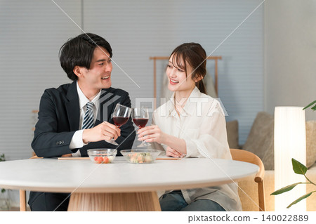 A couple enjoying wine at the dining table in the evening, a couple toasting. A couple enjoying wine at the dining table in the evening, a couple toasting. 140022889