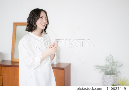 An image of a woman searching for something on her smartphone in her living room at home, reflecting on her worries and thoughts. An image of a woman searching for something on her smartphone in her living room at home, reflecting on her worries and thoughts. 140023449