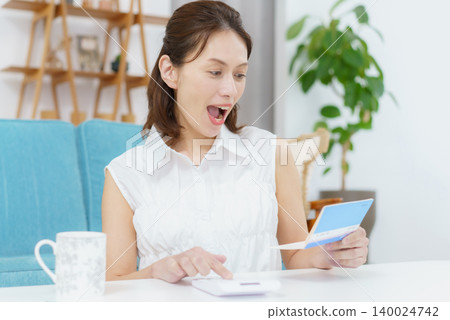 A middle-aged Japanese woman is surprised when she looks at her bank passbook. A middle-aged Japanese woman is surprised when she looks at her bank passbook. 140024742