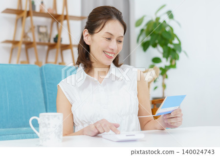 一位中年日本婦女看著她的存摺,臉上露出笑容。 一位中年日本婦女看著她的存摺,臉上露出笑容。 140024743