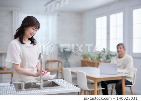 A man and woman in their 60s smiling and talking while wiping dishes in the kitchen 140025031