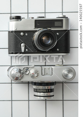 Two vintage cameras placed on a grid tiled surface for viewing Two vintage cameras placed on a grid tiled surface for viewing 140025597