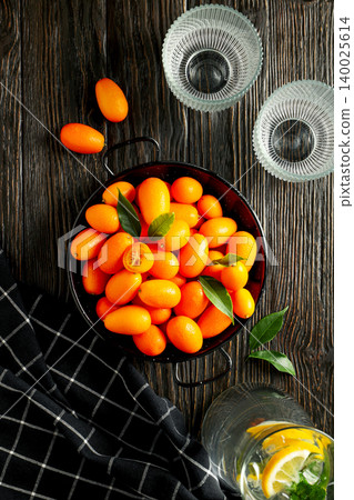Kumquats in a black tray with green leaves and glasses Kumquats in a black tray with green leaves and glasses 140025614
