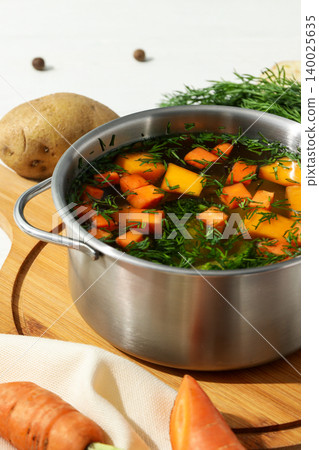 Veggies and herbs simmer in a pot on a wooden board Veggies and herbs simmer in a pot on a wooden board 140025635