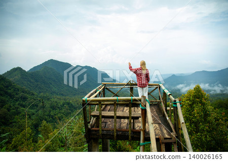 A person stands on a platform overlooking green mountains A person stands on a platform overlooking green mountains 140026165