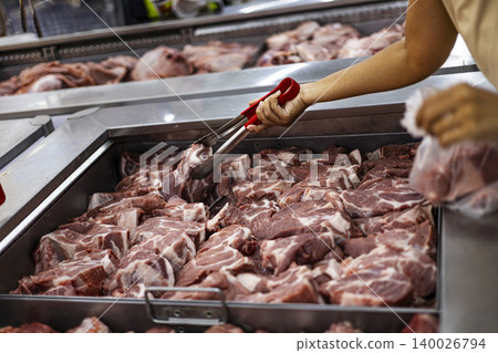 Woman Picking Fresh Pork At A Meat Counter. Close up of a female customer selecting raw pork meat in a grocery store, perfect for food shopping, butchery and cooking ingredient themes. 140026794