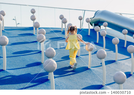Child girl in yellow outfit exploring playground with climbing structures on a sunny summer day. Child girl in yellow outfit exploring playground with climbing structures on a sunny summer day. 140030710